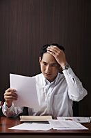 man sitting at desk holding paper looking stressed - Asia Images Group