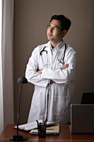 male doctor standing at his desk looking out window - Asia Images Group
