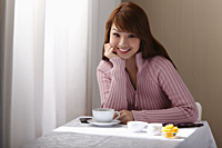 Young woman sitting at table near table with coffee. - Asia Images Group