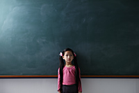 Young girl with pony tails standing in front of a chalk board - Asia Images Group