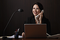 Chinese woman sitting at desk talking on phone and smiling - Asia Images Group
