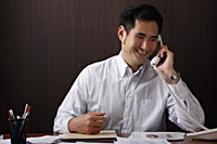 man sitting at desk talking on phone - Asia Images Group