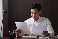 Man sitting at desk looking at paper - Asia Images Group