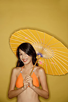 Young woman in bikini, holding umbrella over shoulder, smiling - Asia Images Group