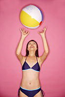 Young woman in bikini, tossing beach ball - Asia Images Group