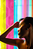 Woman with hand on head, leaning against coloured glass - Asia Images Group
