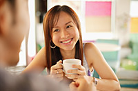 Young woman with mug facing another person, over the shoulder view - Asia Images Group