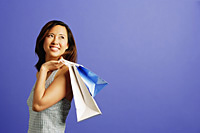 Woman holding shopping bags over shoulder, looking away - Asia Images Group