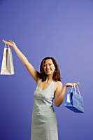 Woman against blue background carrying shopping bags, smiling - Asia Images Group