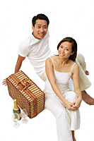 Couple sitting on floor with picnic basket, wine bottle and glasses - Asia Images Group
