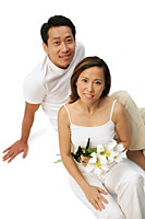 Couple sitting on floor looking at camera, woman holding floral bouquet - Asia Images Group
