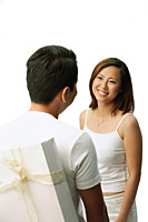 Couple facing each other, man with present behind his back, woman smiling - Asia Images Group
