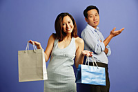 Smiling woman holding shopping bags, sad man behind her with hand raised - Asia Images Group