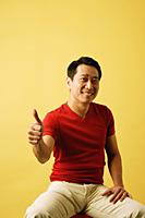Man sitting, looking at camera, making thumbs up sign - Asia Images Group