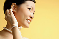 Woman wearing pearl necklace and bracelet, looking away - Asia Images Group