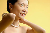 Woman putting on pearl necklace - Asia Images Group