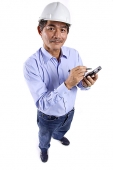 Mature man wearing construction hat, using PDA, looking at camera - Asia Images Group
