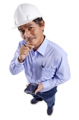 Mature man wearing construction hat, holding PDA, hand on chin, looking at camera - Asia Images Group