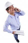 Mature man wearing construction hat, using mobile phone, carrying blueprints - Asia Images Group