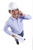 Mature man wearing construction hat, using mobile phone, carrying blueprints, looking at camera - Asia Images Group
