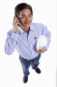 Mature man holding construction hat, using mobile phone - Asia Images Group