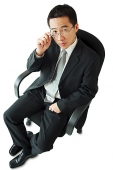 Businessman sitting on office chair, adjusting glasses - Asia Images Group