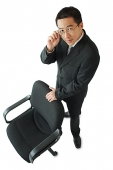 Businessman standing next to office chair, adjusting his glasses, looking at camera - Asia Images Group