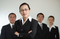 Businesswoman with arms crossed, people in the background - Asia Images Group