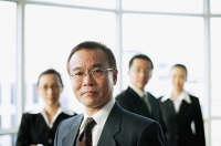 Businessman looking at camera, people in the background - Asia Images Group