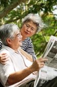 Senior man reading newspaper, woman behind him - Asia Images Group