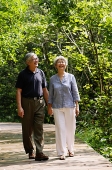 Mature couple walking through park, holding hands, smiling - Asia Images Group