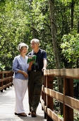 Mature couple standing side by side, talking, woman looking at book - Asia Images Group