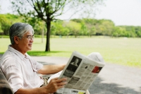 Senior man sitting in park reading newspaper - Asia Images Group