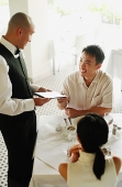 Couple in restaurant, man handing menu back to waiter - Asia Images Group