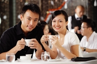 Couple in restaurant, holding cups, smiling at camera - Asia Images Group