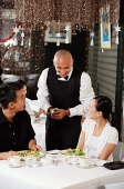 Waiter talking to couple at restaurant - Asia Images Group