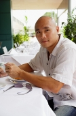 Man sitting at table, holding cup, looking at camera - Asia Images Group