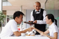 Couple holding hands across the table, waiter standing next to them - Asia Images Group