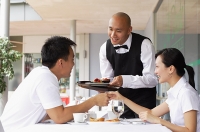 Couple holding hands across the table, waiter serving them - Asia Images Group