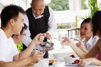 Group of friends having lunch, waiter pouring water at their table - Asia Images Group