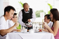 Group of friends at restaurant eating, waiter pouring water at their table - Asia Images Group