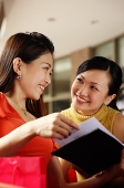 Two women looking at each other, one holding book - Asia Images Group