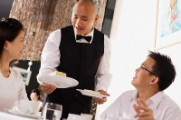 Waiter serving plates of dessert  to customers in restaurant - Asia Images Group