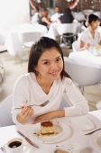 Woman at table in restaurant, dessert in front of her, smiling at camera - Asia Images Group