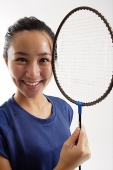 Woman holding badminton racket next to her face, smiling - Asia Images Group
