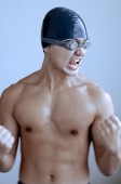Man wearing swimming cap and goggles, making fists and grimacing - Asia Images Group