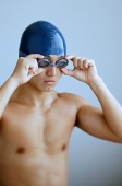 Man adjusting goggles, wearing swimming cap - Asia Images Group