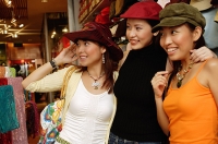 Women shopping, trying on hats, looking away - Asia Images Group