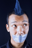 Man with mohawk, mouth taped shut, looking away - Asia Images Group