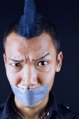 Man with mohawk, mouth taped shut, looking at camera, eyebrow raised - Asia Images Group